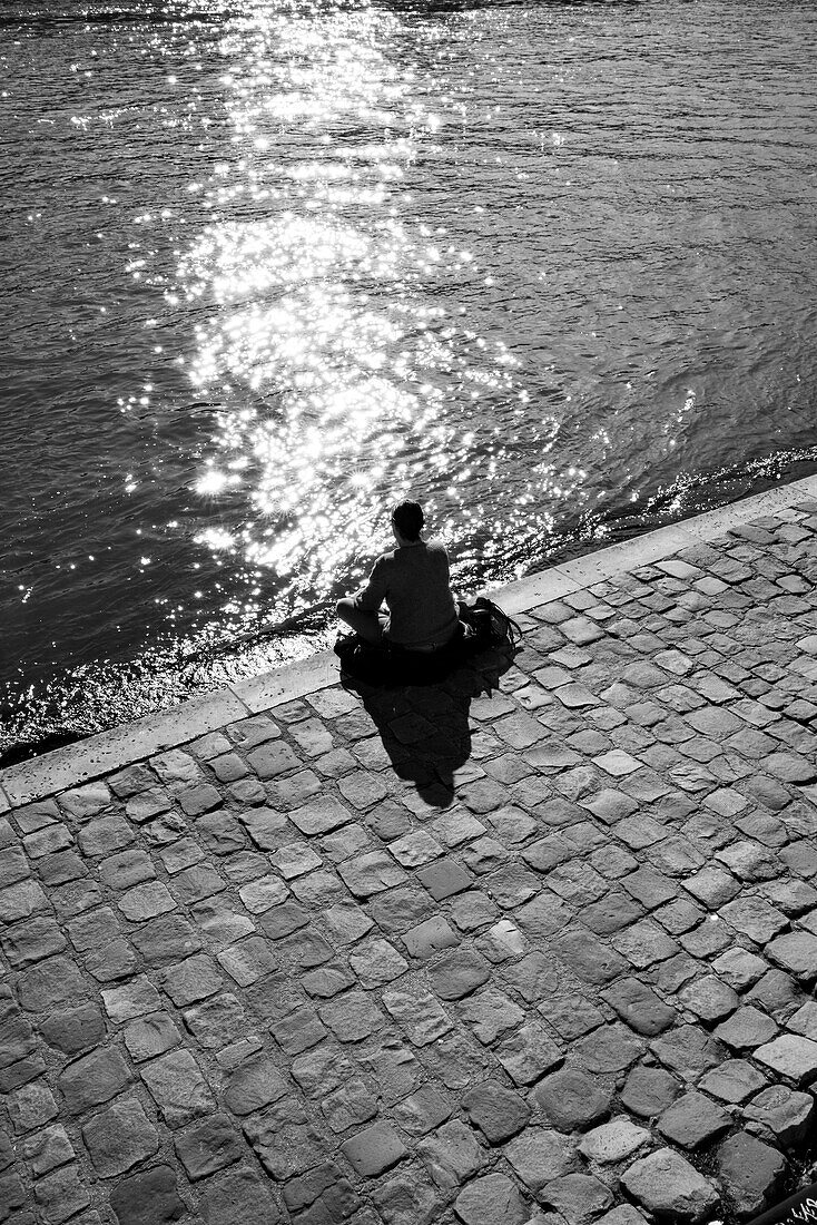 Mann sitzt am Ufer der Seine in Paris, Frankreich.