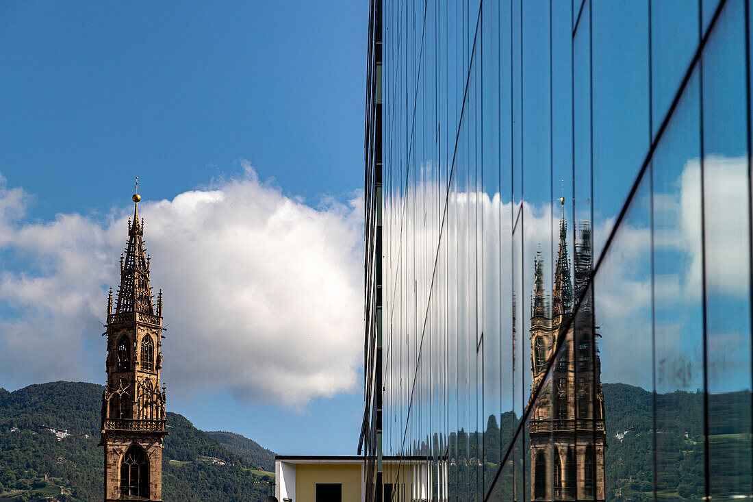 Glockenturm des Dom spiegelt sich in einem Glasgebäude wider, unter bewölktem Himmel Bozen, Südtirol, Italien