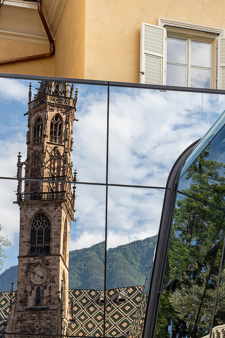 Glockenturm des Dom spiegelt sich in einem Glasgebäude wider, unter bewölktem Himmel Bozen, Südtirol, Italien