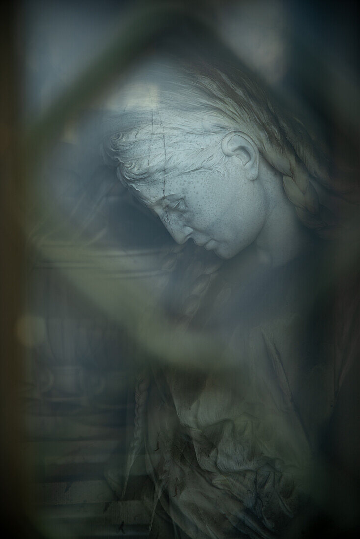 Statue einer Frau, die in einen Schrein auf einem Friedhof in Gent herabblickt.