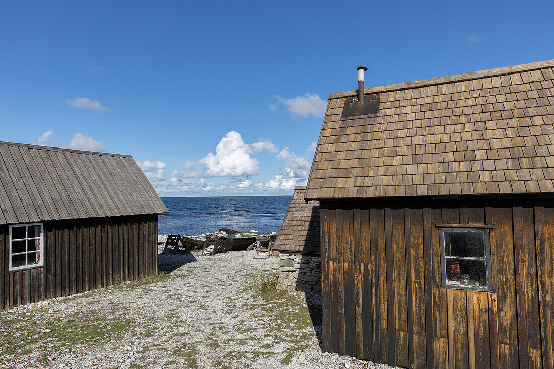 Blick zwischen zwei Fischerhütten auf altes kleines Fischerboot am Kieselstrand, Farö, Gotland, Schweden.