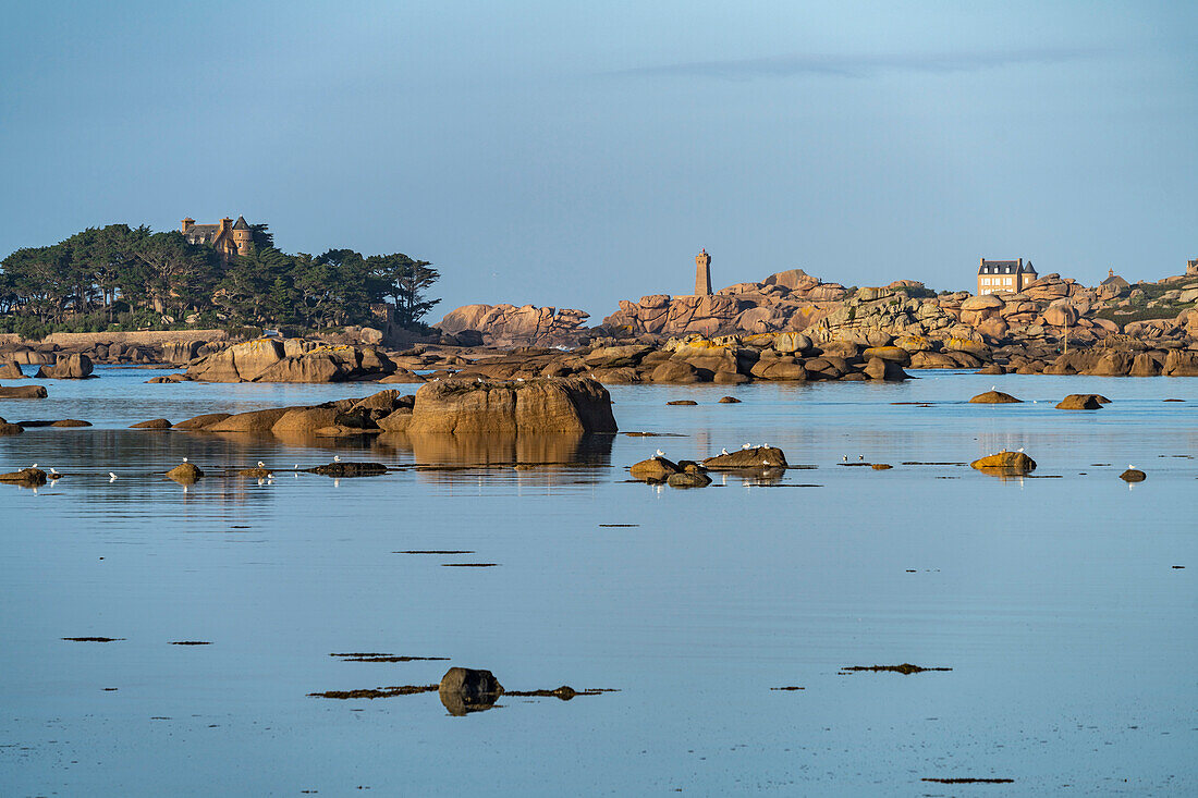 The rocks of the pink granite coast Côte de Granit Rose at the Baie de Sainte Anne near Tregastel looking towards the Maison Gustave Eiffel and the Phare de Ploumanac'h lighthouse , Brittany, France