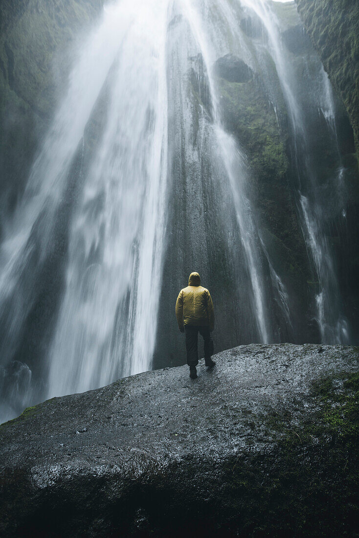 Man wearing yellow raincoat by Seljalandsfoss waterfall in Iceland