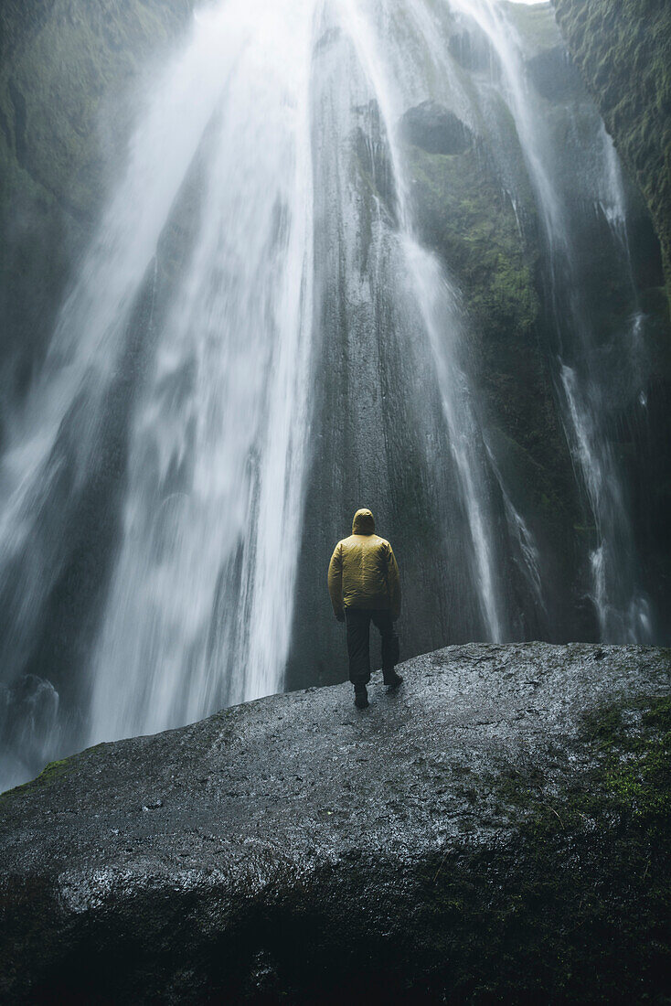 Mann mit gelbem Regenmantel am Wasserfall Seljalandsfoss in Island