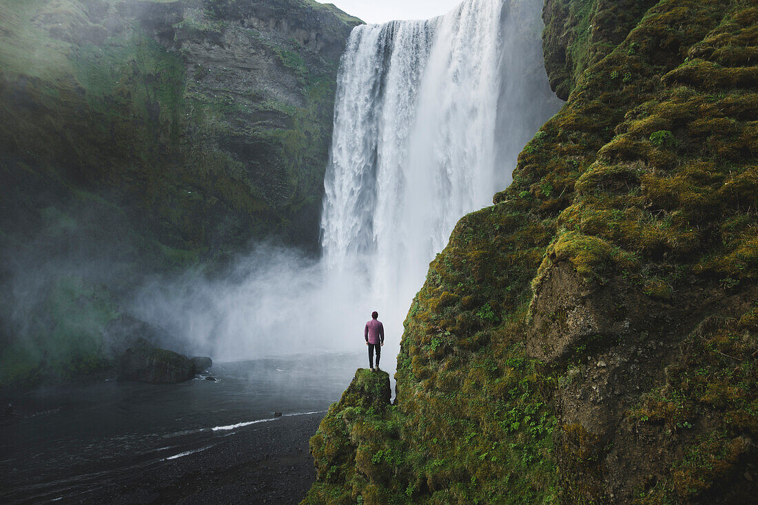 Mann, der am Skogafoss-Wasserfall in Island steht