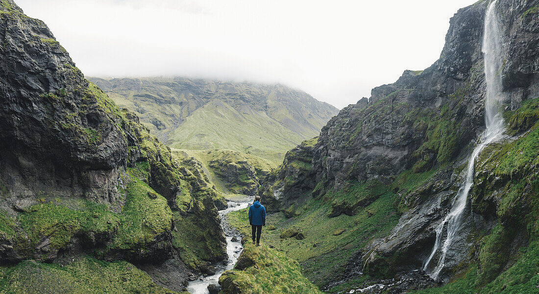 Mann, der durch Wasserfall in Island wandert