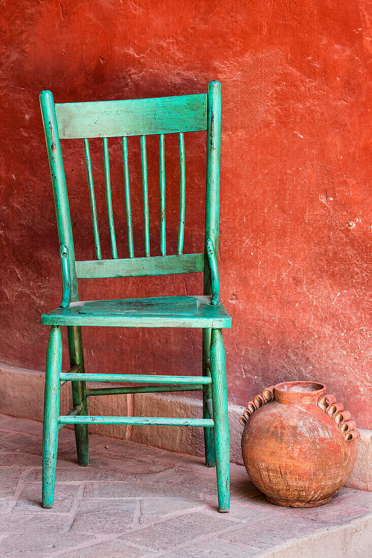 Mexiko, San Miguel de Allende. Ein leerer Stuhl und ein Terrakottatopf auf einer farbenfrohen Veranda.