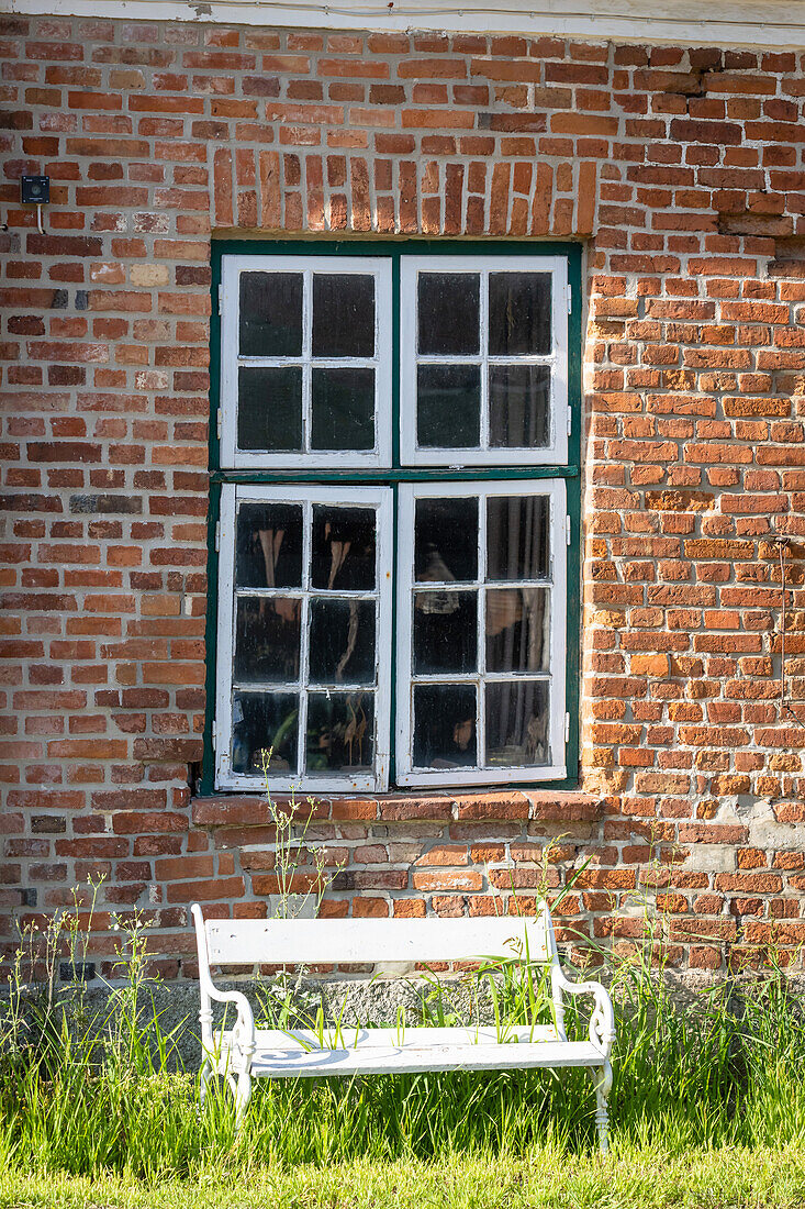White garden bench in front of a barn window and red brick historic vintage
