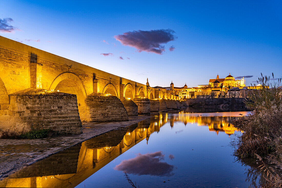 Römische Brücke über den Fluss Río Guadalquivir und die Mezquita - Catedral de Córdoba in der Abenddämmerung, Cordoba, Andalusien, Spanien  