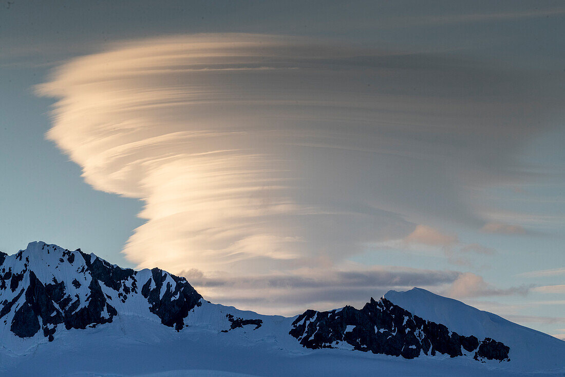 Shorefast ice and snow covered mountains with a lenticular cloud build up in Wilhamena Bay, Antarctica, Polar Regions