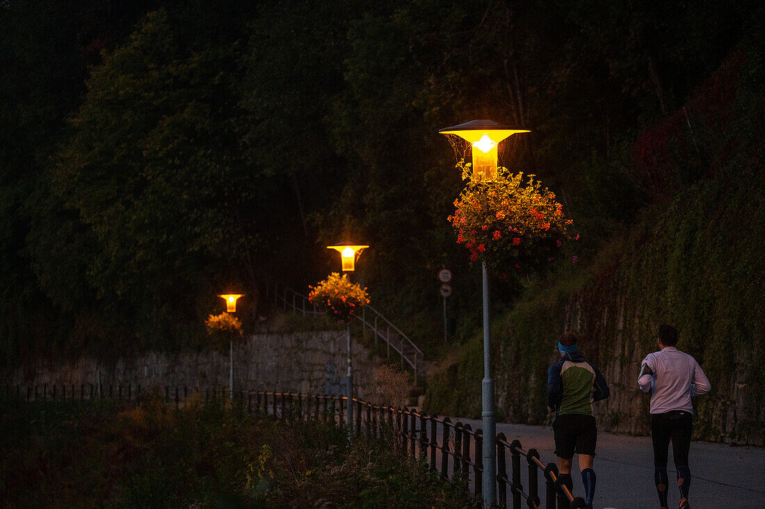 Zwei Läufer am frühen Morgen mit Straßenbeleuchtung, Salzachkai in Obendorf, Salzburg, Österreich