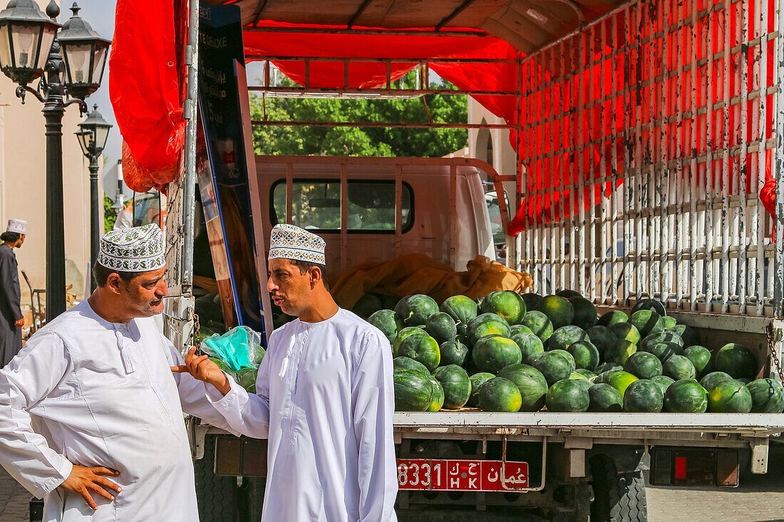Zwei Männer verhandeln vor einem offenen Transporter mit Melonen am Souk in Nizwa, Oman, Arabische Halbinsel, Asien
