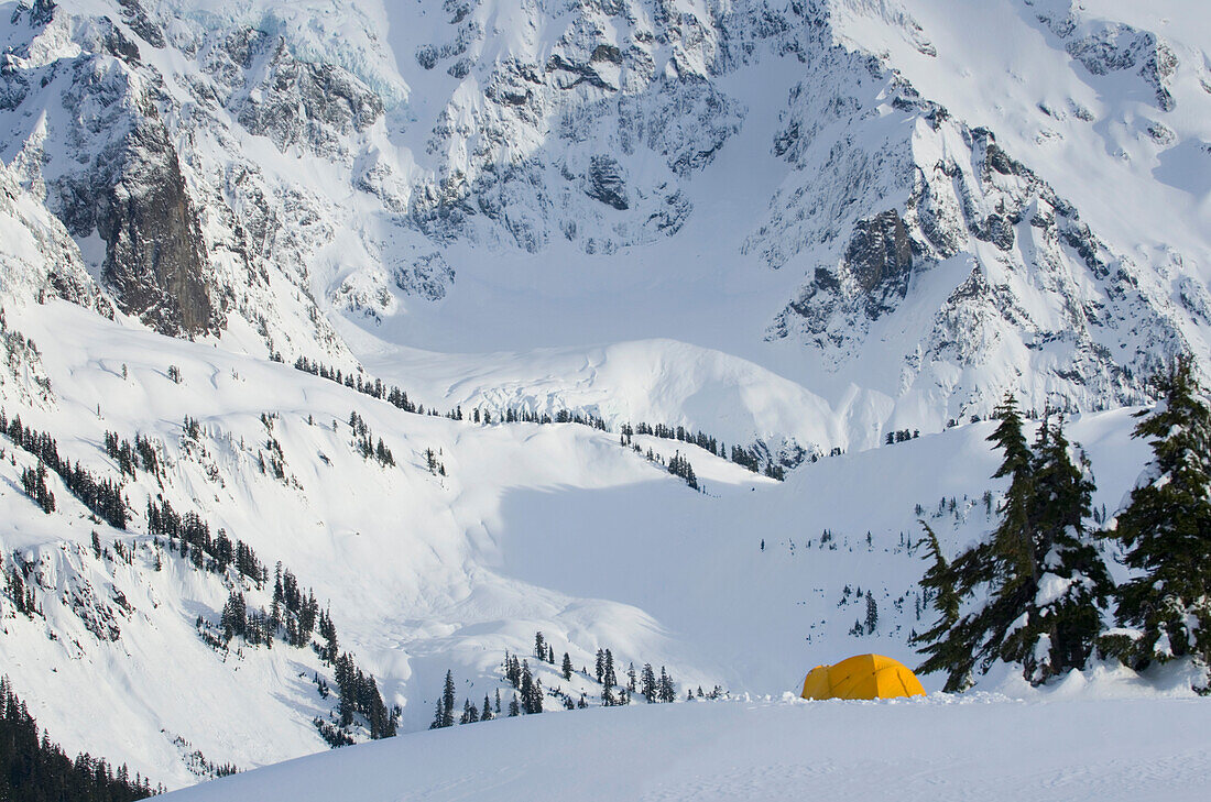 Ein kleines gelbes Zelt im Tiefschnee an einem Hang, Blick auf die steilen Hänge der Berge.