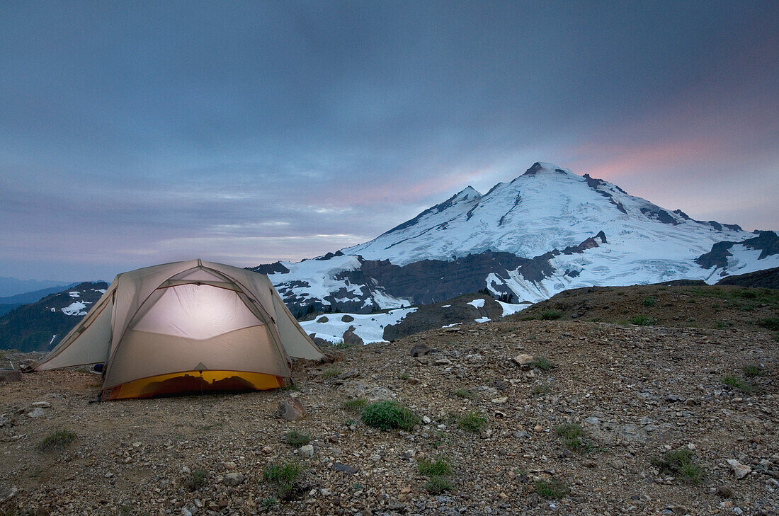 A small tent pitched on a screen slope just below the snowline, at sunset in the Mount Baker wilderness.