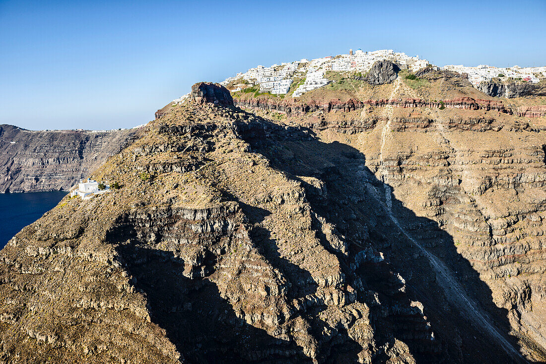 The cliffs and rock formations of an island in the Aegean sea, with a town of white-washed houses on the top of the cliffs.