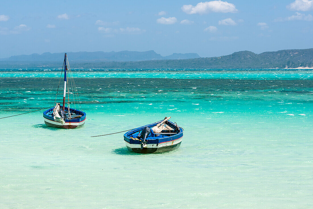Two fishing boats moored in the shallows on a beach, turquoise sea and mountains.
