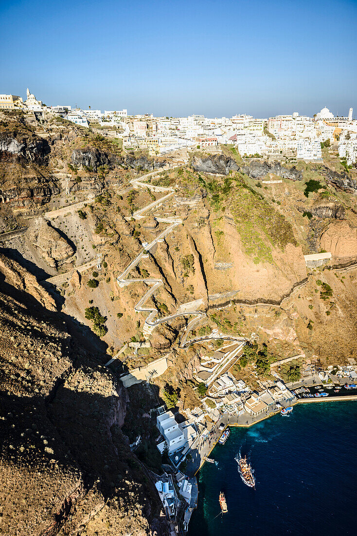 Luftaufnahme einer Stadt an der Spitze einer steilen Klippe auf der Insel Egeo und dem gewundenen Pfad zu den Häusern vom Landepunkt an der Küste.