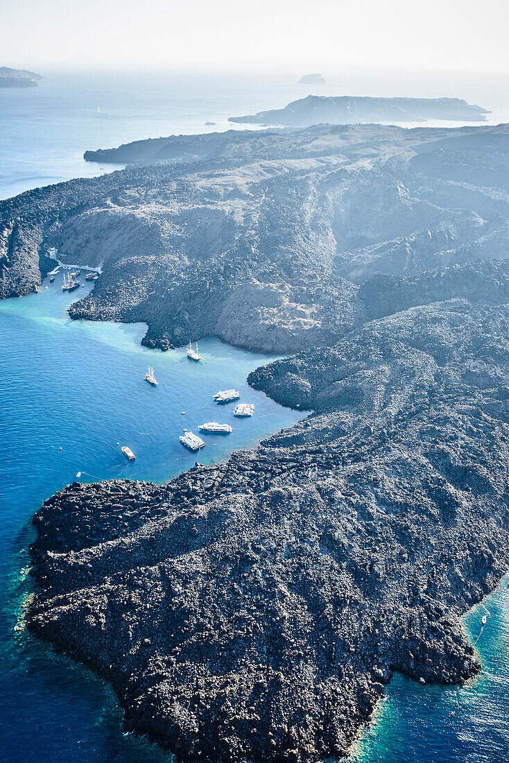 Luftaufnahme der Landschaft einer Insel in der Caldera, Vulkangestein und steile Klippen und geschützte Anlegestellen mit Booten.
