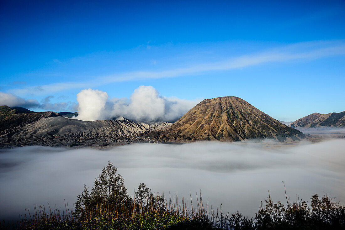 Mount Bromo volcano, a somma volcano and part of the Tengger mountains range, the cone rising above low cloud in the landscape.
