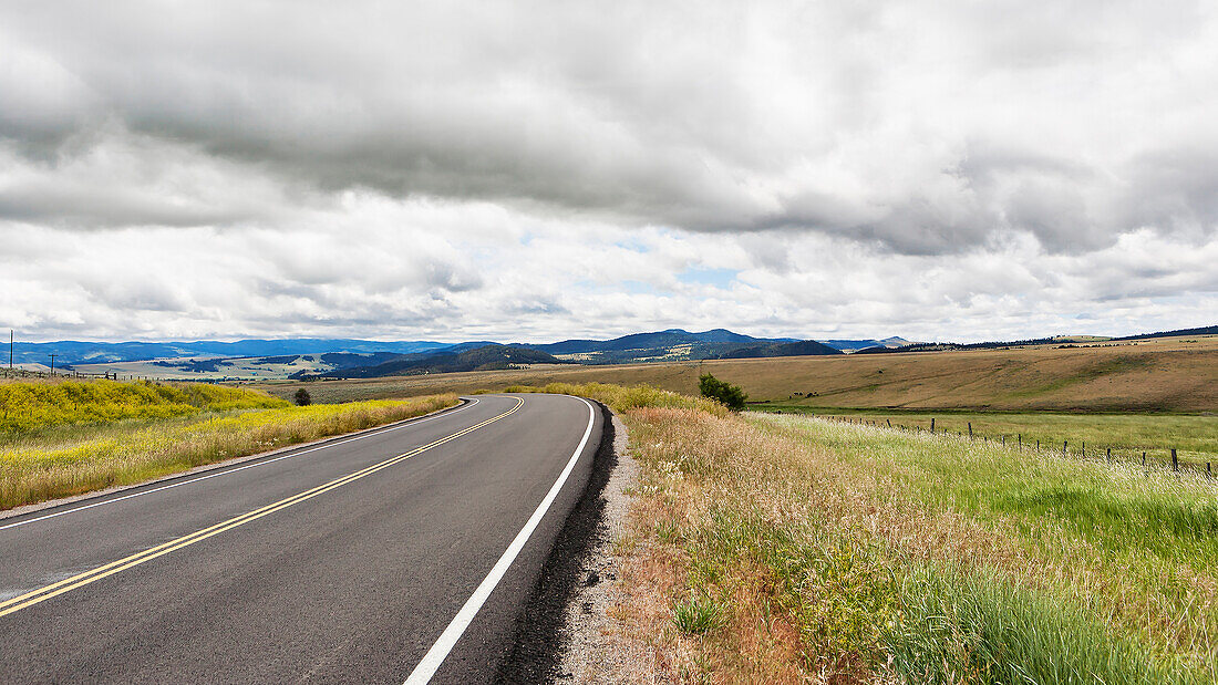 Eine asphaltierte Straße durch eine flache Landschaft mit Hügeln und Ackerland, Montana, USA