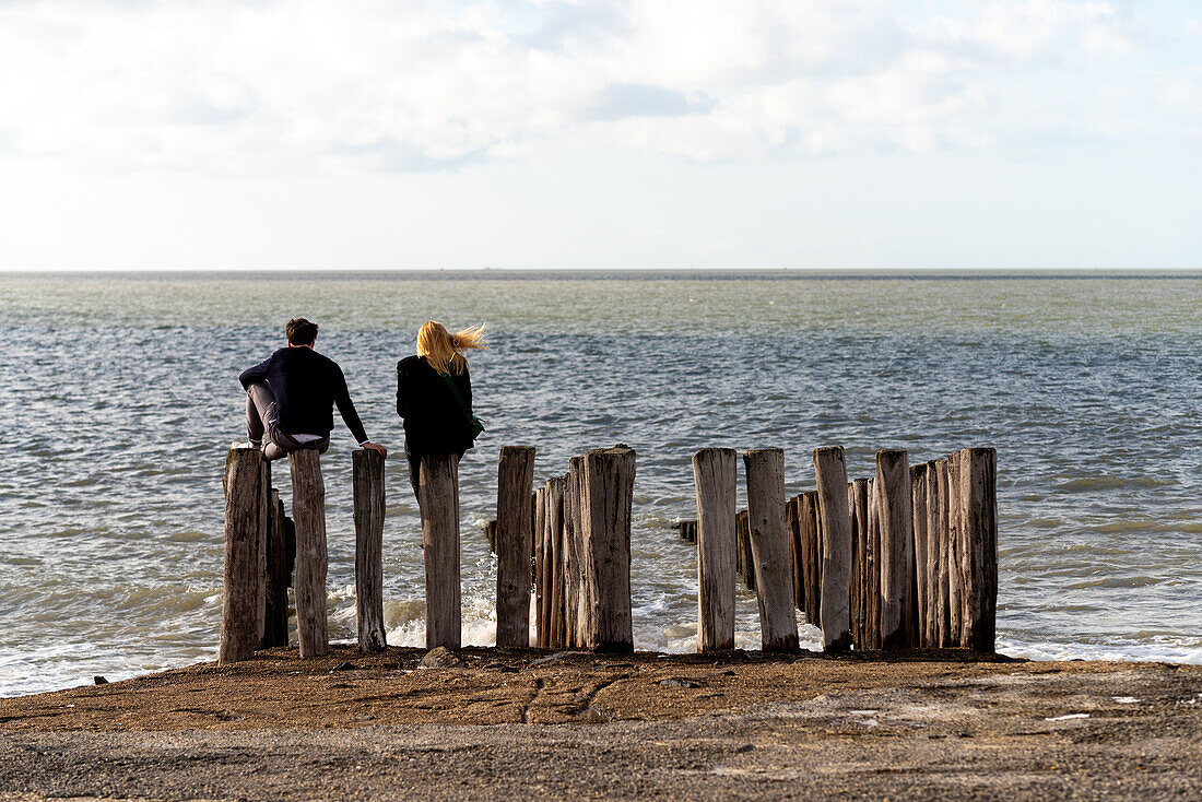 Ein Paar sitzt auf Wellenbrecher, Strand von Groede in der Provinz Zeeland, Niederlande