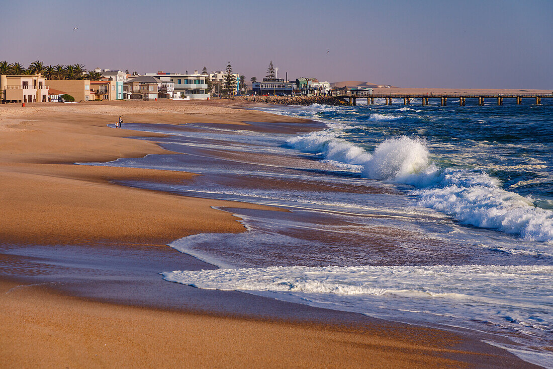 The beach with crashing waves at the jetty in Swakopmund in Namibian Africa at sunset