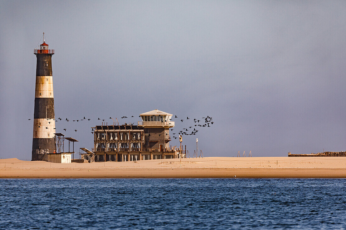 The lighthouse and Pelican Point Lodge with birds on a sandbank off Walvis Bay, Namibia, Africa