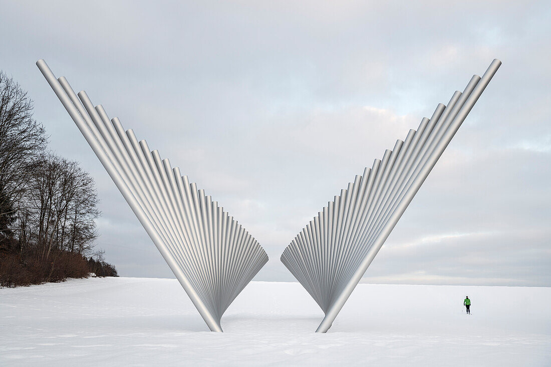 Woman with cross-country skis next to the sculpture Narrow and Wide Horizon in a wintry landscape, Mundingen near Ehingen, Alb Donau district, Swabian Alb, Baden-Württemberg, Germany