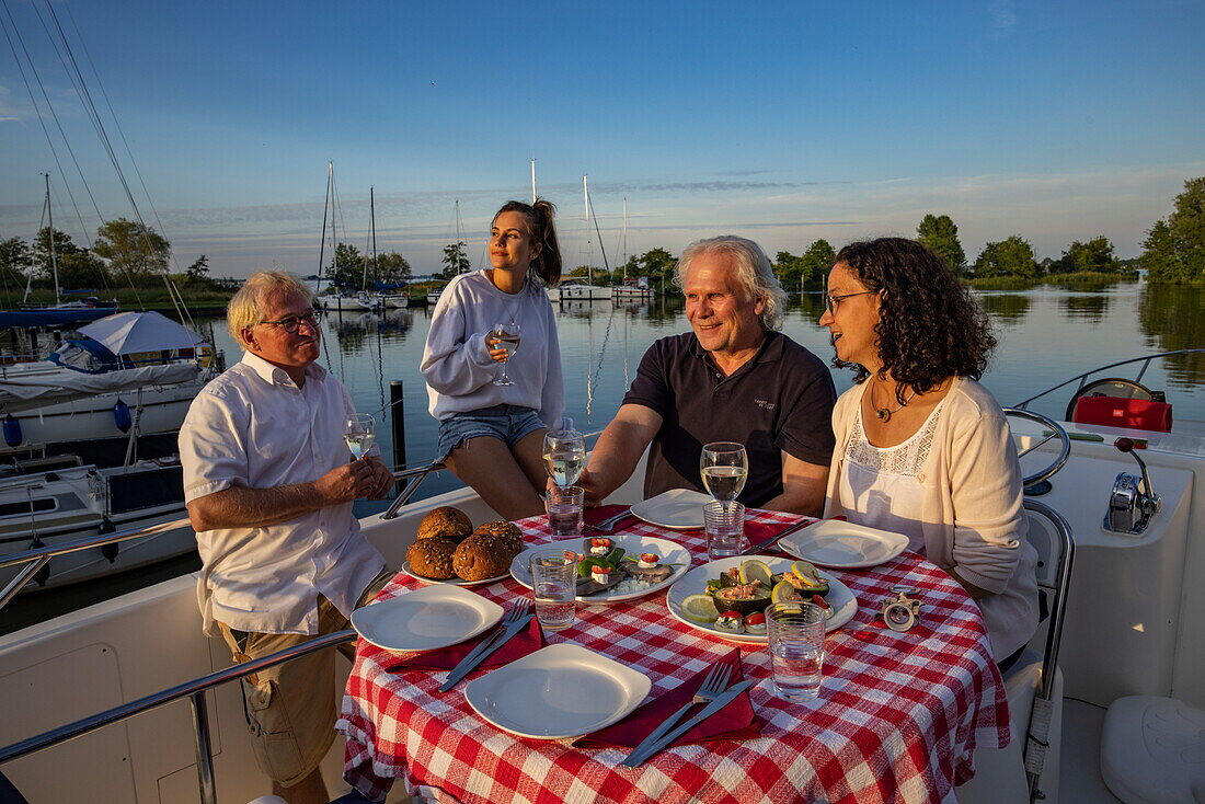 Friends enjoy dinner on the deck of a Le Boat Elegance houseboat moored on the island of Nieuwe Kruispolle in Lake De Fluezen, near It Heidenskip, Friesland, The Netherlands, Europe