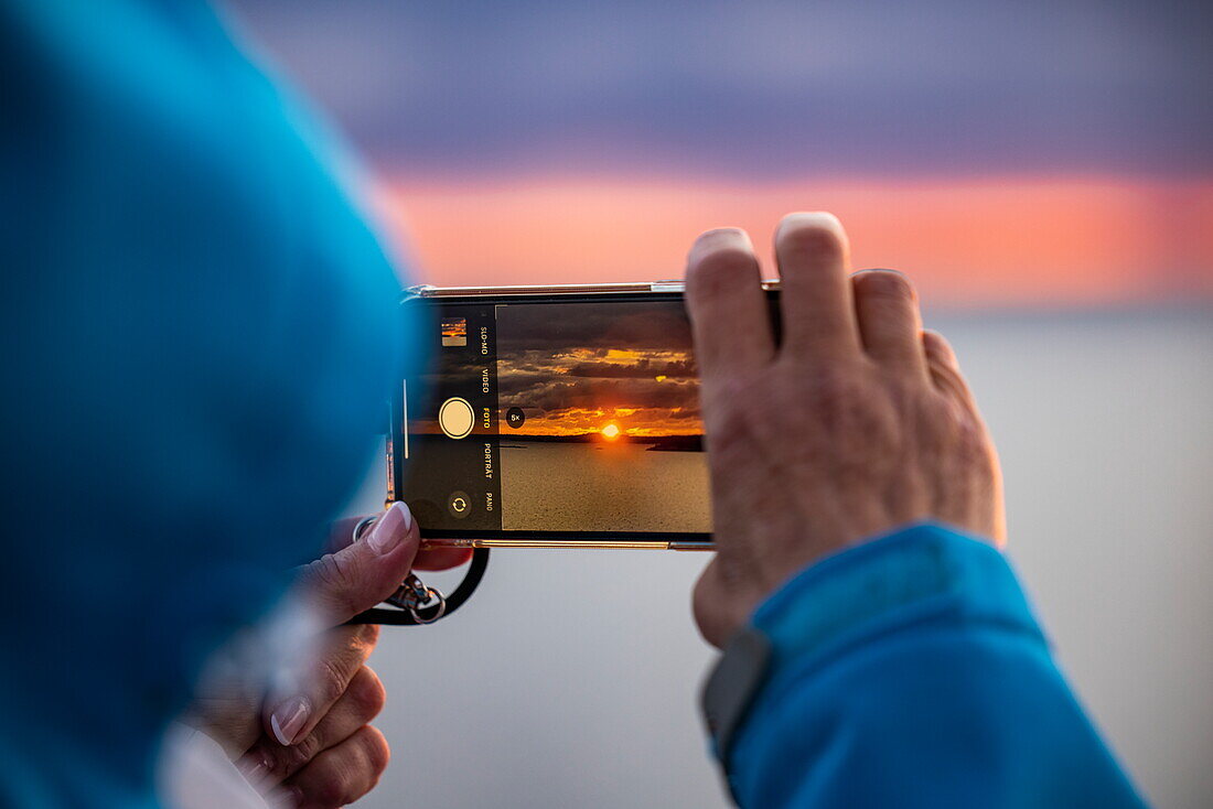Frau macht Sonnenaufgangsfoto mit Smartphone in den Stockholmer Schären, Stockholmer Schären, in der Nähe von Stockholm, Schweden, Europa