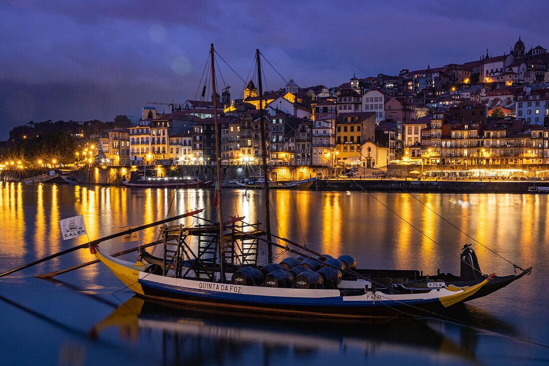 Traditionelles Portwein-Transportboot auf dem Fluss Douro mit Blick auf die Altstadt von Ribeira und das historische Zentrum in der Abenddämmerung, Vila Nova de Gaia, Porto, Portugal, Europa