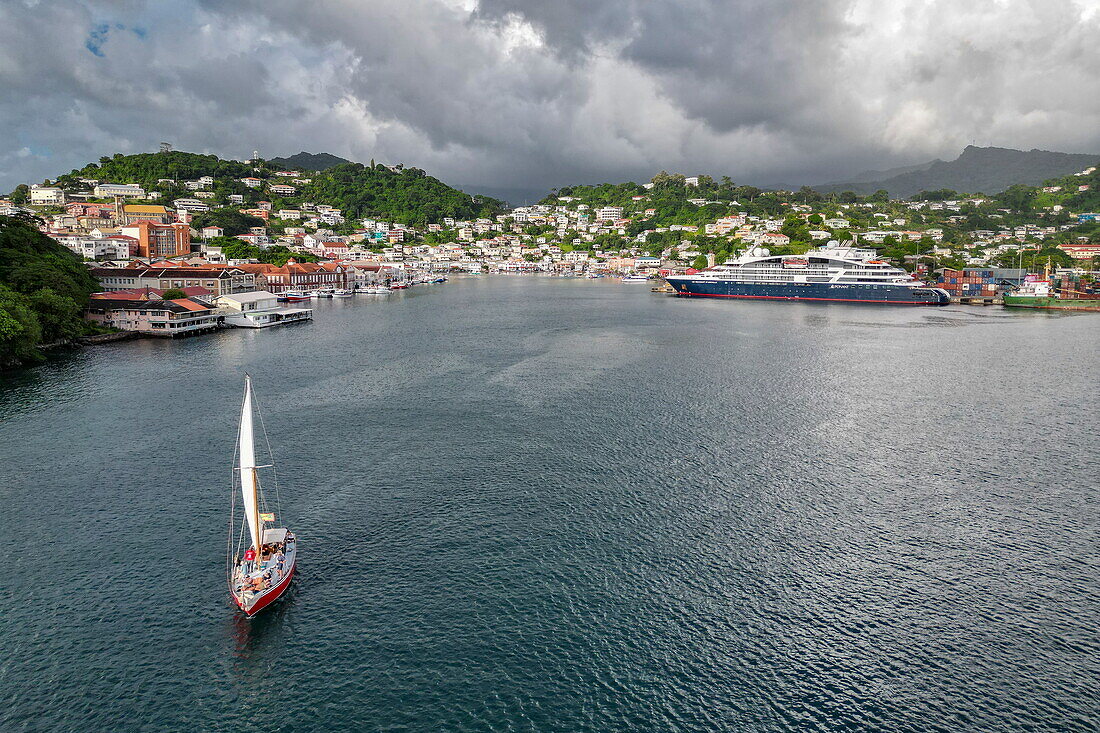 Luftaufnahme des alten Segelboot Carriacou (Savvy Sailing) in der St. George's Bay mit Kreuzfahrtschiff Le Dumont D'Urville (Ponant Cruises) am Pier im Hafen von St. George, Saint George's, Grenada, Karibik
