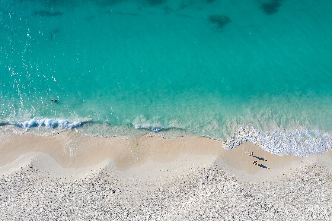 Luftaufnahme von zwei Personen, die am schönen Eagle Beach am Wasser entlang spazieren, Eagle Beach, Aruba, Karibik