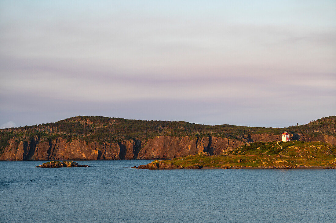 Canada, Labrador, Newfoundland, Trinity, Sea coastline with distant?Fort Point Lighthouse at sunset