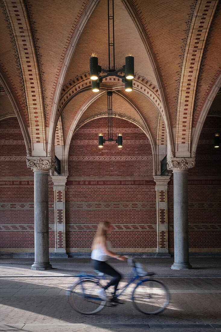 Frau auf Fahrrad fährt durch Portal des Reichsmuseum (Rijksmuseum), Amsterdam, Provinz Noord-Holland, Niederlande, Europa