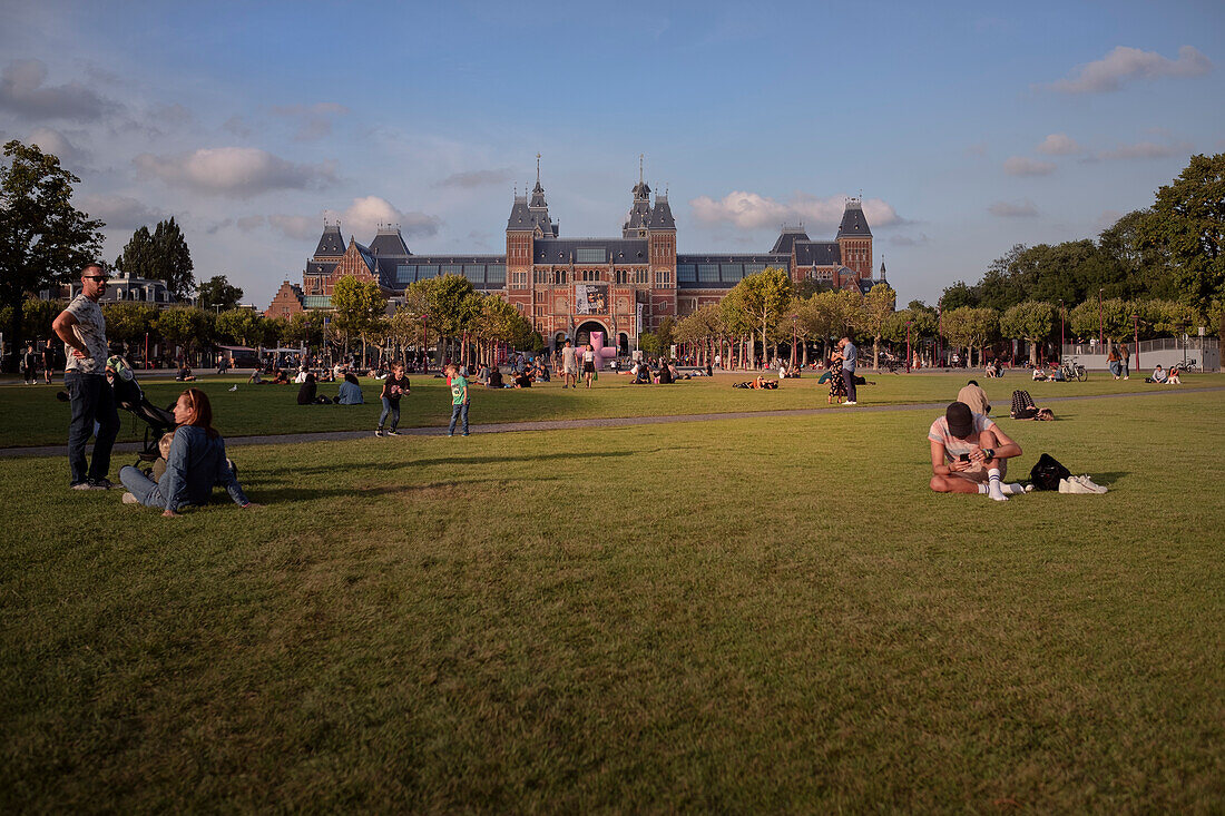 Menschen sitzen im Gras des Museumplein vor dem Reichsmuseum (Rijksmuseum), Amsterdam, Provinz Noord-Holland, Niederlande, Europa