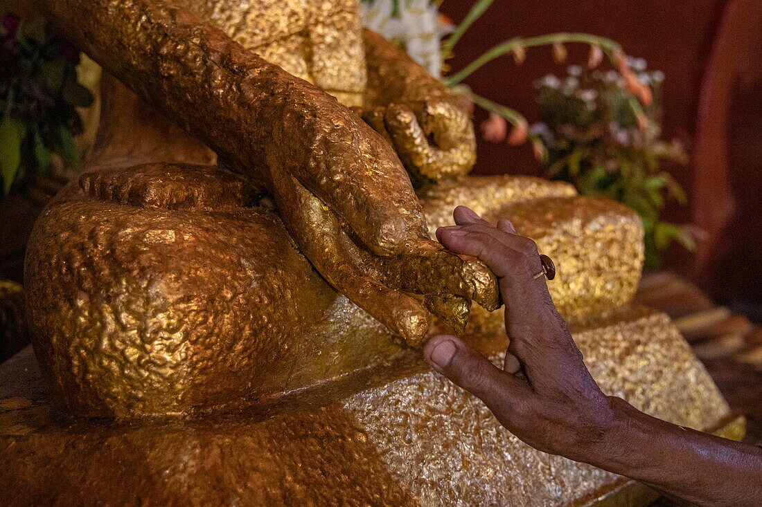 A worshiper's hand places gold leaf on the Buddha statue at Ananda Temple, Old Bagan, Nyaung-U, Mandalay Region, Myanmar, Asia
