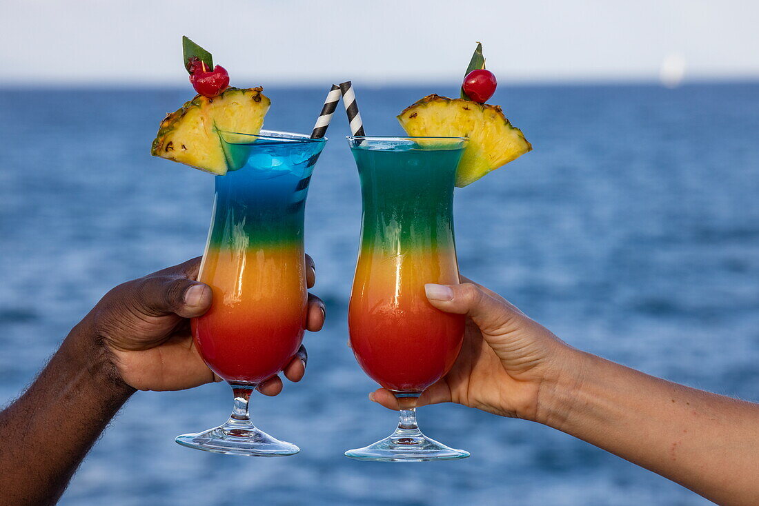 Hände halten bunte Cocktails, in der Nähe der Insel Mahé, Seychellen, Indischer Ozean