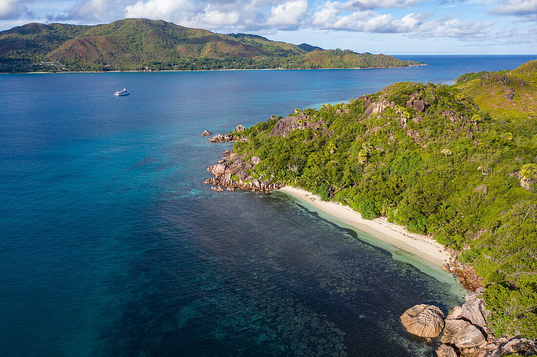 Luftaufnahme von Strand in einer kleinen Bucht mit Granitfelsen und Boutique-Kreuzfahrtschiff M/Y Pegasos (Variety Cruises) in der Ferne, Insel Curieuse, Seychellen, Indischer Ozean