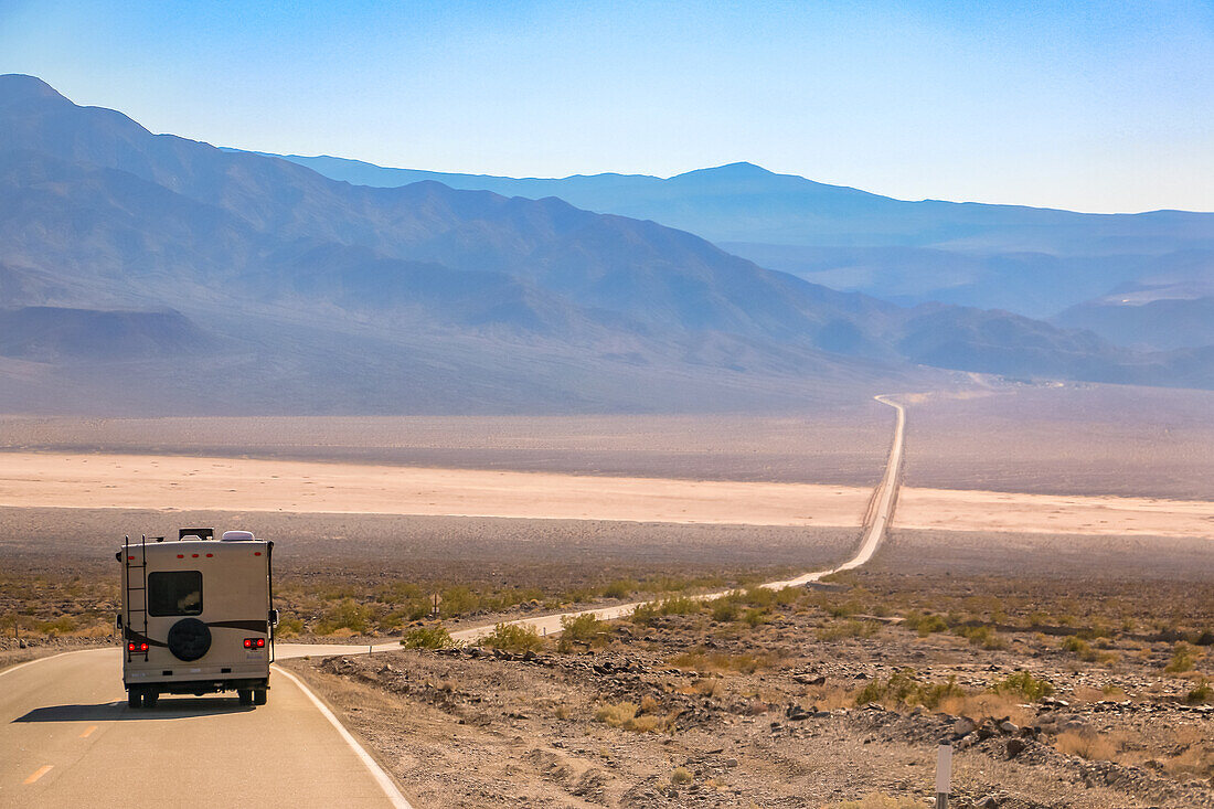 A lone motorhome travels the Nadeau Trail through the hot plateau in Death Valley in California, USA