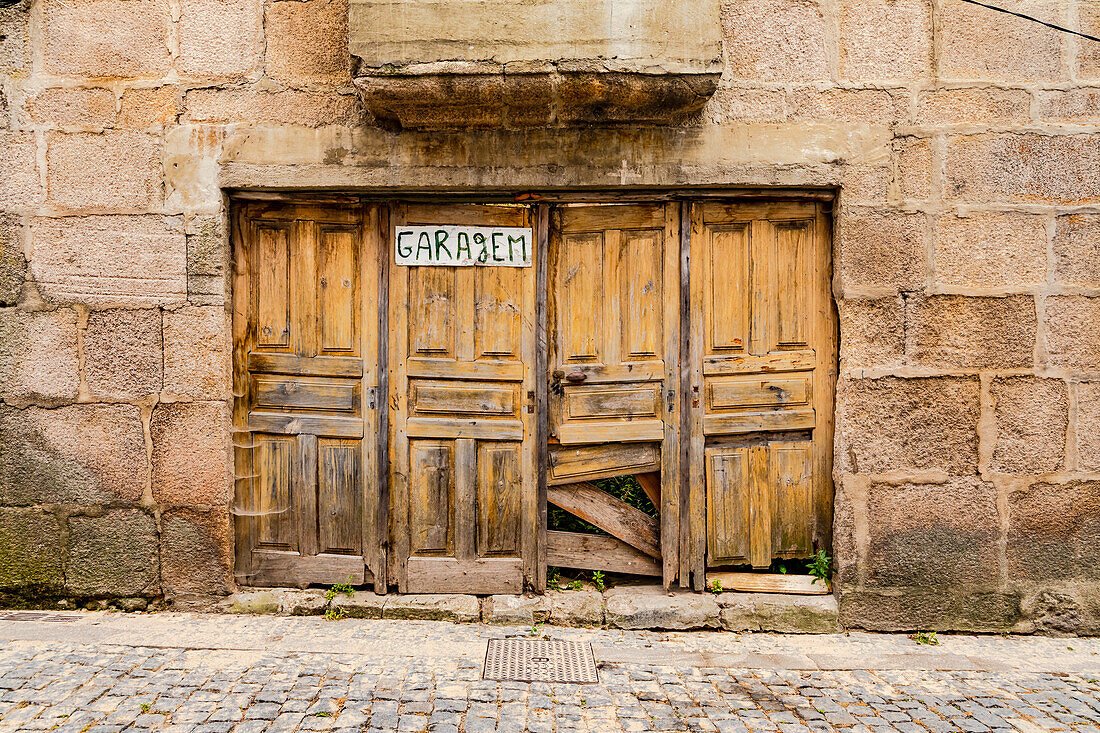 Rotten wooden double doors on a derelict garage on the facade of a stone house, Lamego, Portugal