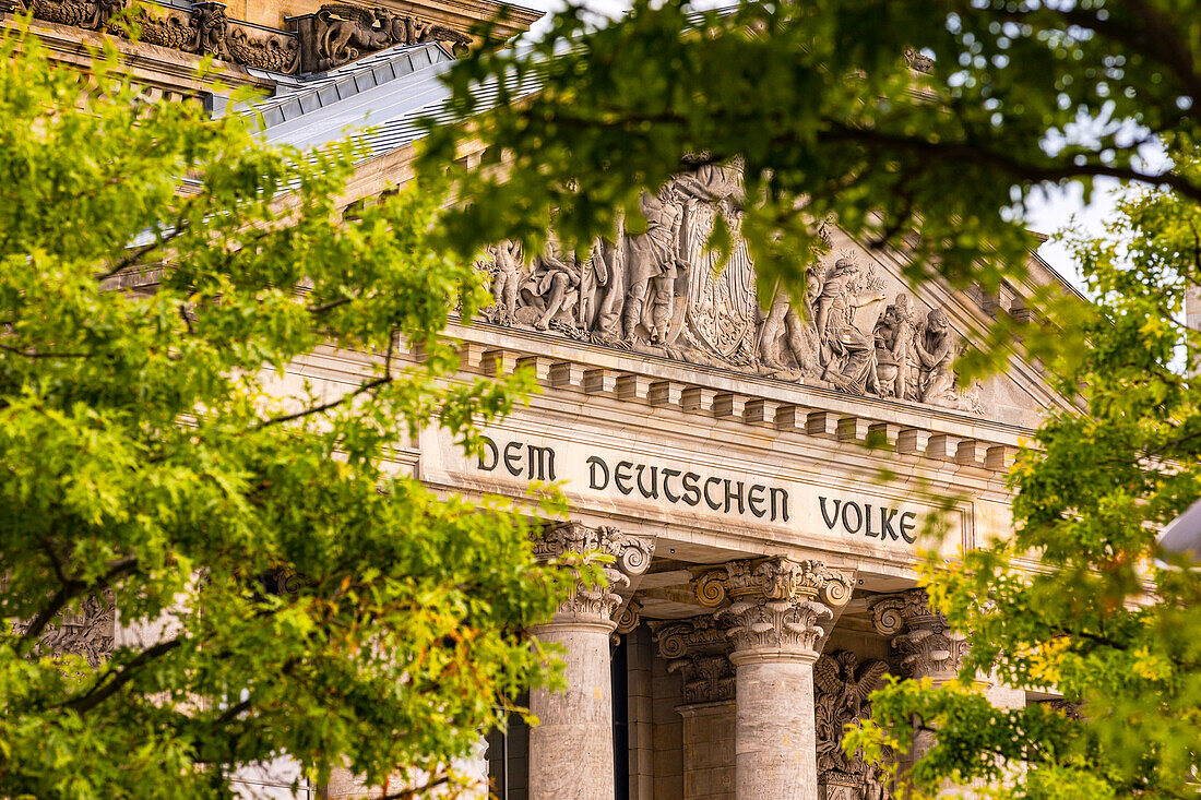 Die Inschrift Dem Deutschen Volke auf dem Architrav im Westportal vom Reichstag Gebäude zwischen Bäumen gesehen, Berlin, Deutschland