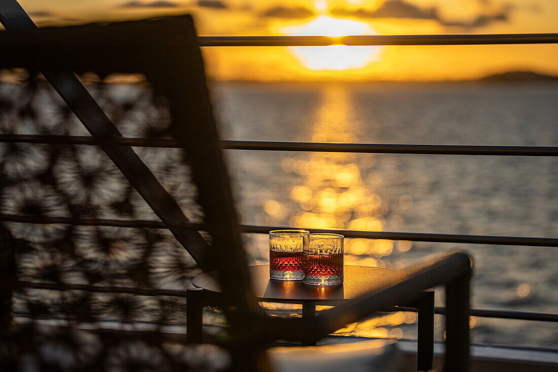 Zwei Cocktailgläser, gesehen durch einen Liegestuhl bei Sonnenuntergang, Paridas-Inseln, Golf von Chiriqui, Panama, Mittelamerika