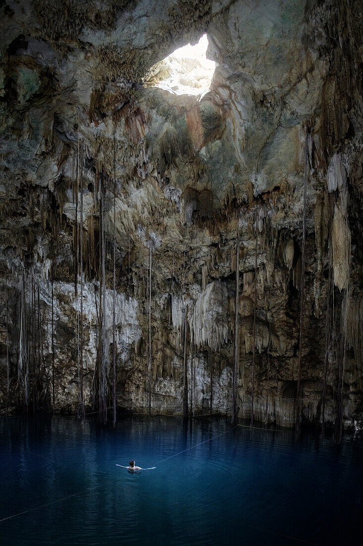 Woman swimming in Cenote Xkeken near Valladolid looking at hole in rock cap, Yucatan, Mexico, North America, Latin America