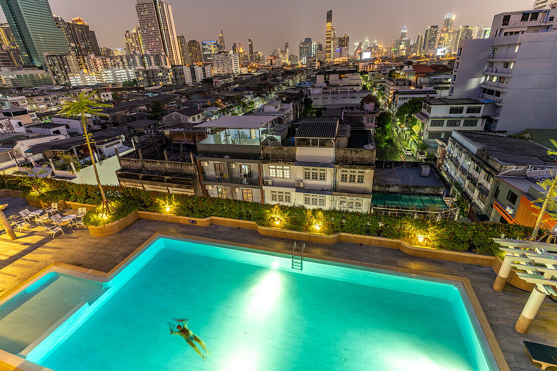Illuminated swimming pool in front of Bangkok city view and skyline at dusk, Thailand, Asia