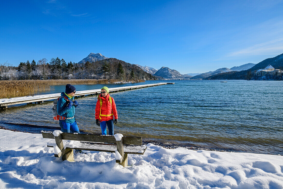 Man and woman hiking standing at bench on the shore of Lake Fuschl, Fuschlsee, Salzkammergut, Salzkammergut Mountains, Salzburg, Austria