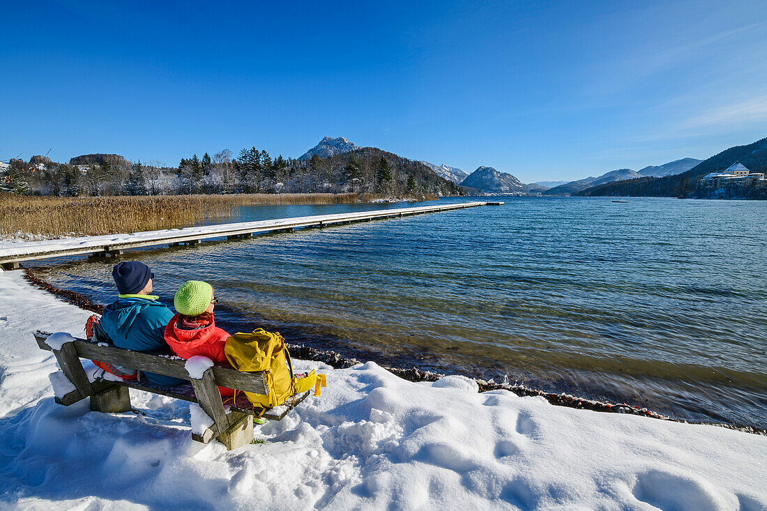 Mann und Frau beim Wandern sitzen auf Bank und blicken auf Fuschlsee, Fuschlsee, Salzkammergut, Salzkammergutberge, Salzburg, Österreich