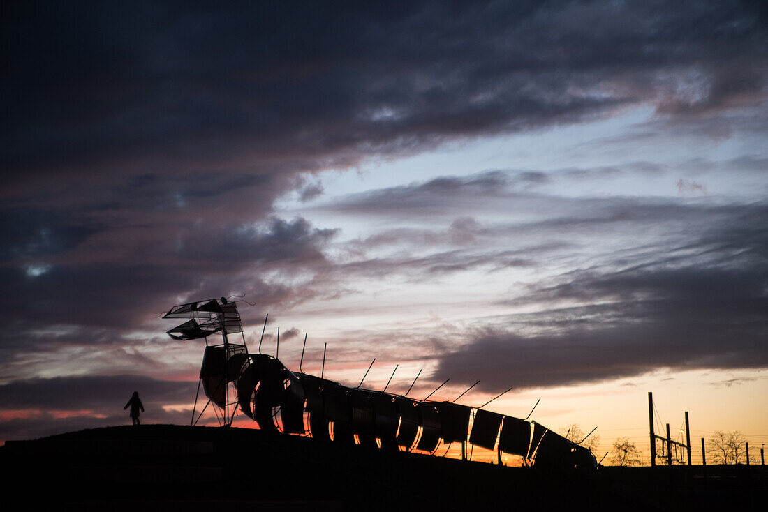 Metal sculpture of a dragon on a hill in the light of dusk.