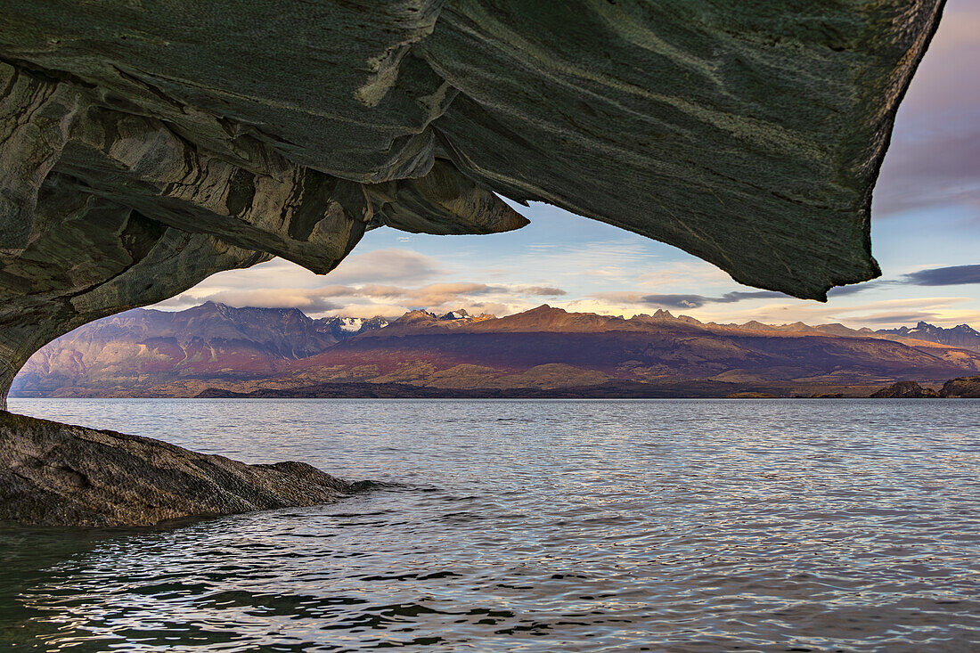 Ausblick auf die Berge der Anden durch eine Marmorformation der Cuevas de Marmol im Lago General Carrera, Chile, Patagonien, Südamerika