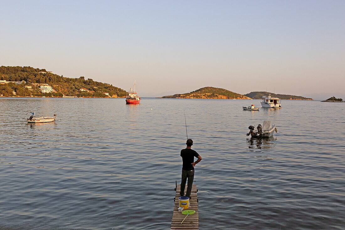 Junger Mann fischt im Hafenbecken von Skiathos Stadt, Insel Skiathos, Nördliche Sporaden, Griechenland
